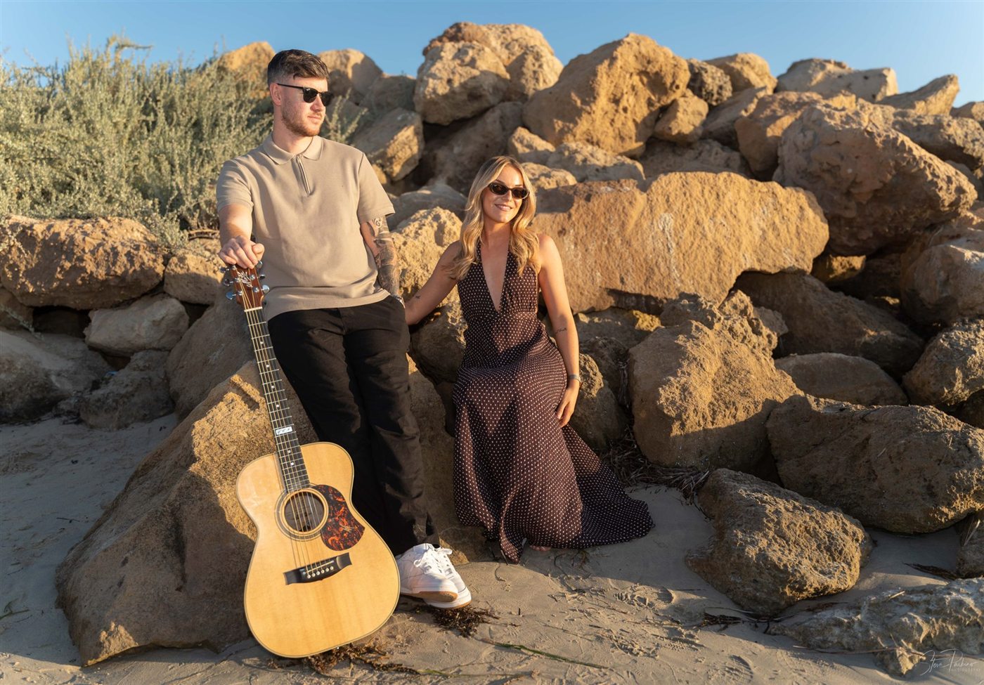 Two On A Visa sitting by rocks with an acoustic guitar
